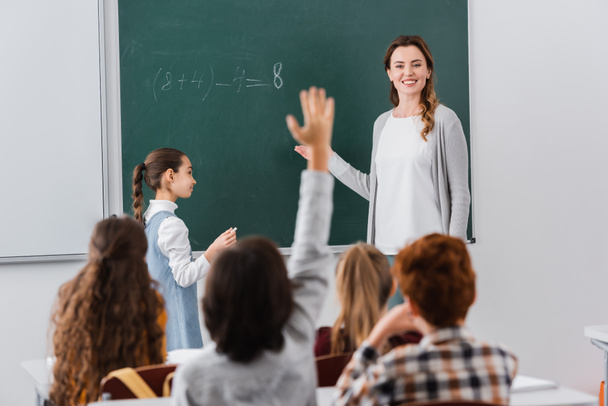 insegnante sorridente guardando scolaro alzando la mano su primo piano sfocato - Foto, immagini