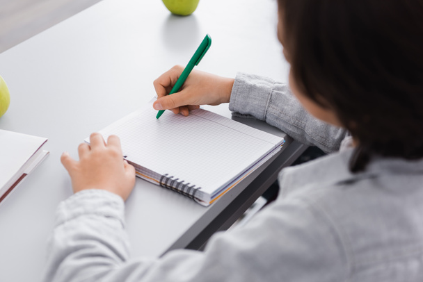 estudante escrevendo com caneta no caderno durante a aula na escola, foreground borrado - Foto, Imagem