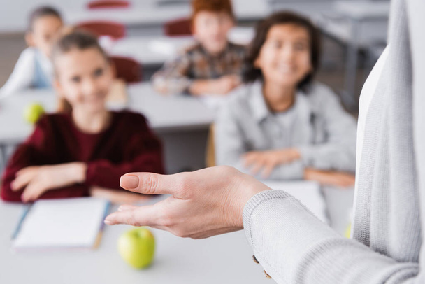 leraar gebaren tijdens les in de buurt van schoolkinderen op wazig achtergrond - Foto, afbeelding