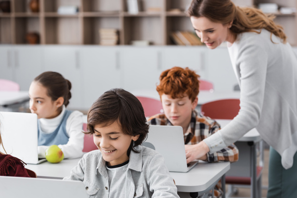 insegnante aiutare scolaro lavoro su laptop durante lezione, sfondo sfocato - Foto, immagini