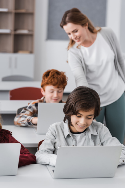 teacher standing near schoolboy working on computer during lesson, blurred background - Φωτογραφία, εικόνα