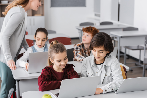 leraar in de buurt van schoolkinderen werken op laptops in de klas - Foto, afbeelding