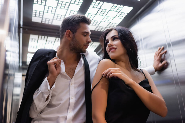 Sensual woman standing near boyfriend with jacket in elevator  - Photo, Image