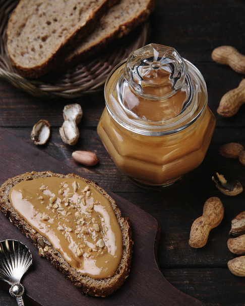 Organic Peanut Butter in Glass Jar with Peanuts in Shell on Wooden Background. Healthy Breakfast Vegetarian Food Concept. - Photo, Image