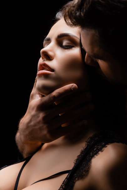 Young man touching chin of sexy woman with closed eyes isolated on black - Photo, Image