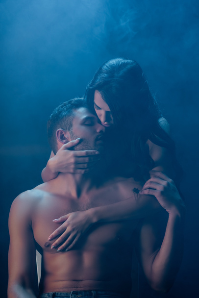 Jovem mulher abraçando namorado apaixonado no fundo preto com fumaça  - Foto, Imagem
