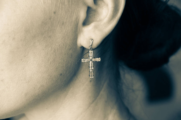 Pendiente en forma de cruz en la oreja de una mujer, de cerca - Foto, imagen