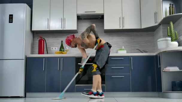 Mies, joka on töissä siivousfirmassa, siivoaa keittiön lattian ja tanssii. - Materiaali, video