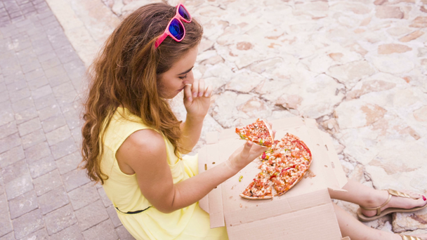 vrouw eten een pizza zittend in de straat - Video