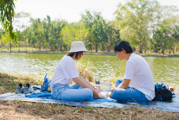 Ασιατικό πικ-νικ ζευγάρι με αίσθημα ευτυχίας στο πάρκο με τη λίμνη την άνοιξη - Φωτογραφία, εικόνα