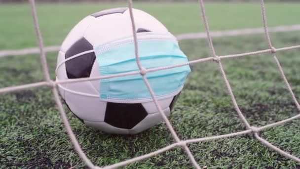 スタジアムの緑の草の上の医療マスクでサッカーボール。ゴールネットのボール。サッカー競技会が中止 - 映像、動画