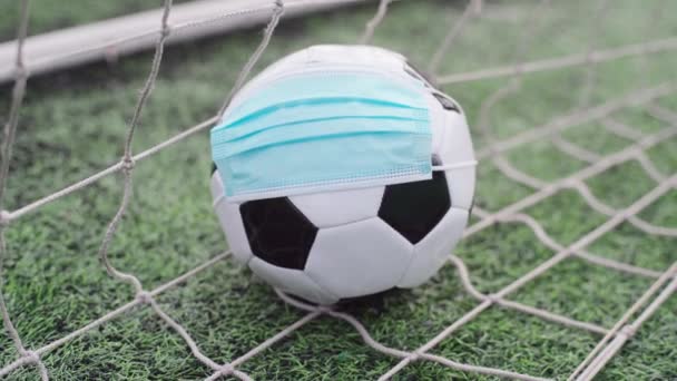 Soccer Ball in Medical Mask on Stadium Green Grass. Ball in Goal Net. Football Competitions Stopped - Footage, Video
