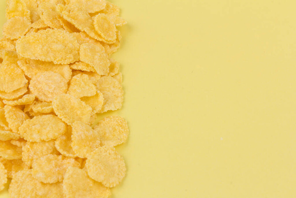 Yellow cornflakes on yellow  background. Traditional breakfast yellow cereal, a healthy lifestyle. - Photo, Image
