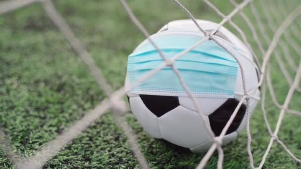 スタジアムの緑の草の上の医療マスクでサッカーボール。ゴールネットのボール。サッカー競技会が中止 - 映像、動画