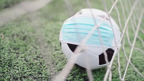 Ballon de football en masque médical sur herbe verte du stade. Balle dans Goal Net. Interruption des compétitions de football - Séquence, vidéo