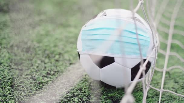Ballon de football en masque médical sur herbe verte du stade. Balle dans Goal Net. Interruption des compétitions de football - Séquence, vidéo