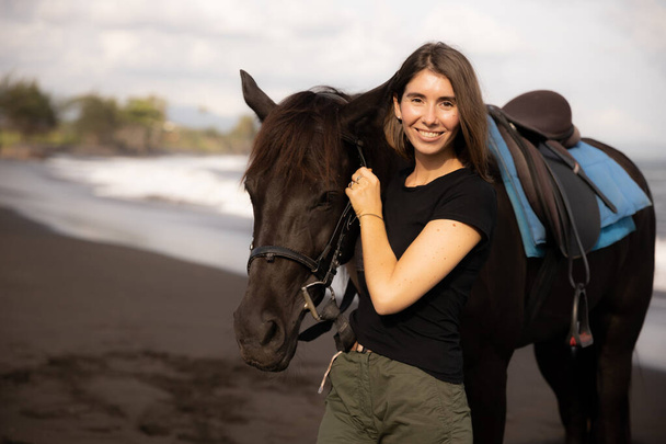 Portrait of happy woman and brown horse. Young Caucasian woman hugging horse. Romantic concept. Love to animals. Nature concept. Bali, Indonesia - Photo, Image