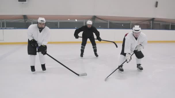 Zpomalený zoom-in záběr mužských hokejistů v uniformách a helmách stojící v postoji s holí na prázdné ledové aréně při pohledu do kamery - Záběry, video