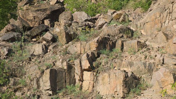 放棄された花崗岩の採石場のロッキー斜面。まばらな植生で生い茂った鋭い石。様々な岩. - 写真・画像