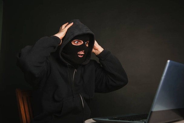 Небезпечний маскований хакер з капюшоном не може проникнути на сервери даних і заразити їх вірусами. Зловив злочинця через ноутбук. Фото на темному тлі в студії
 - Фото, зображення
