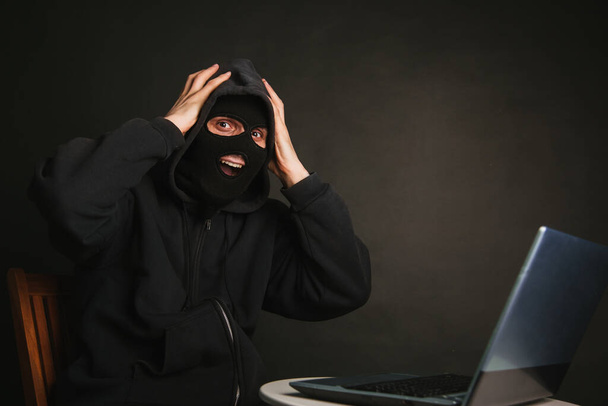 Un pericoloso hacker mascherato con un cappuccio non può infiltrarsi nei server di dati e infettarli con virus. Ha preso il criminale attraverso un portatile. Foto su sfondo scuro in studio - Foto, immagini