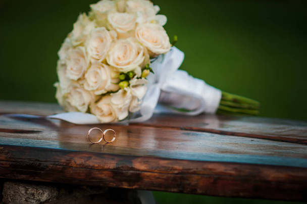 Обручальные кольца на деревянном подставке на фоне букета невесты - Фото, изображение