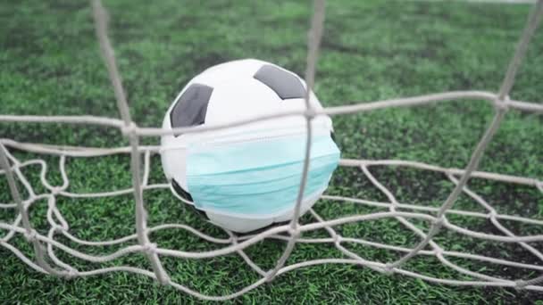 Футбольный мяч в медицинской маске на стадионе Грин Грасс. Мяч в сетке ворот. Футбольные соревнования прекратились - Кадры, видео
