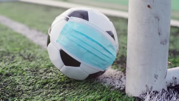 Black and White Soccer Ball in Medical Mask Lying Near Soccer Goal. Prázdný stadion. Fotbal během karantény. Zrušení fotbalových soutěží - Záběry, video