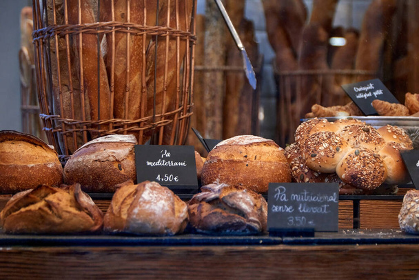 Variado surtido de panes artesanales en la ventana de una panadería de la ciudad con precios y nombres en catalán. - Foto, Imagen