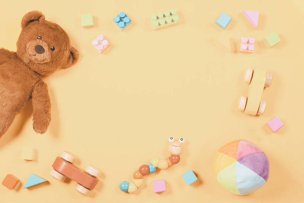 Marco de juguetes para niños bebé con oso de peluche, coche de juguete de madera, ladrillos de colores sobre fondo de color amarillo - Foto, Imagen