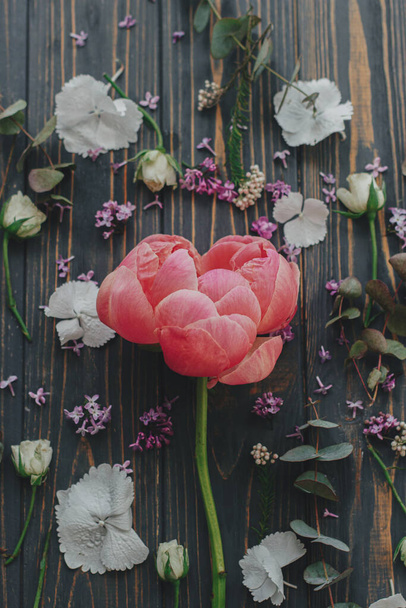 Hermosa peonía rosa y lila, eucalipto, hortensias, pétalos de rosa sobre fondo de madera oscura tendido plano. Vista superior. Diseño de flores de primavera en madera rústica. - Foto, imagen