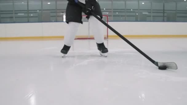 Alacsony-szakasz lövés felismerhetetlen férfi hoki játékos korcsolyázik az üres jégarénában csöpögő korong felé mozgó kamera - Felvétel, videó