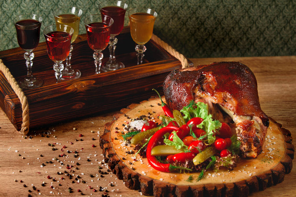 Costeleta de porco com picles, salada, legumes, pimenta em uma tábua de madeira contra o fundo de copos com álcool. - Foto, Imagem