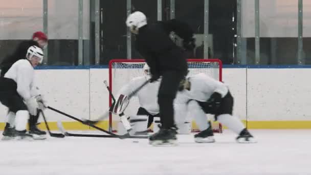 Täysi laukaus aktiivinen uros jääkiekkoilijat pelipaidat ja kypärät yrittää hallita jääkiekkoa kaukalossa, kun maalivahti odottaa net - Materiaali, video