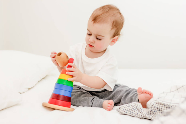 Cute baby boy playing colorful pyramid tower on white bed. - Photo, Image
