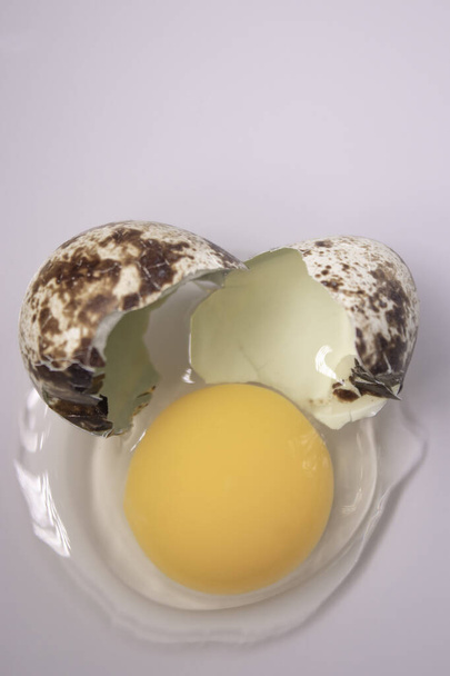 разбитое перепелиное яйцо на белом фоне с протекающими белыми и желтками. здоровой сырой пищи. - Фото, изображение
