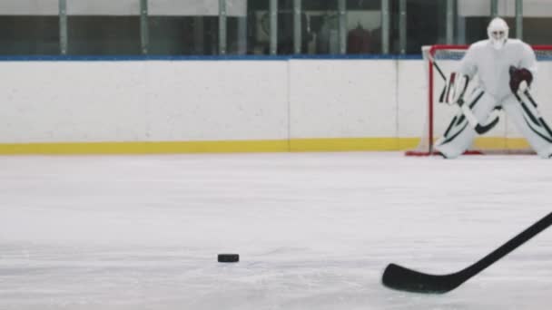 Low-angle achteraanzicht PAN met traagheid van mannelijke hockey spelers proberen te scoren doel in keepers poort staking puck met stok. Goalie vangen puck met succes - Video