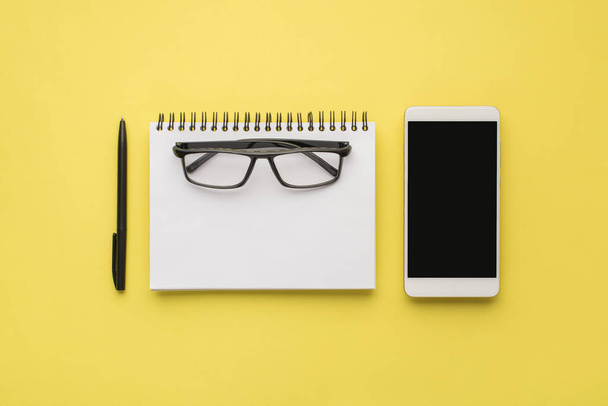 Photo overhead of notebook phone and black pen isolated on the yellow background - Photo, Image