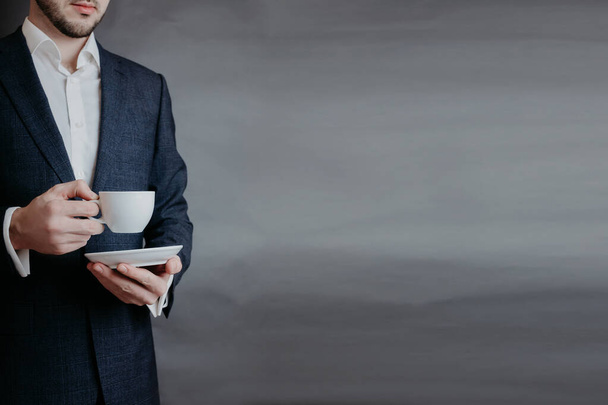 Isolated photo of businessmen in suit holding the cup of coffee on the grey background for copyspace. - Photo, Image