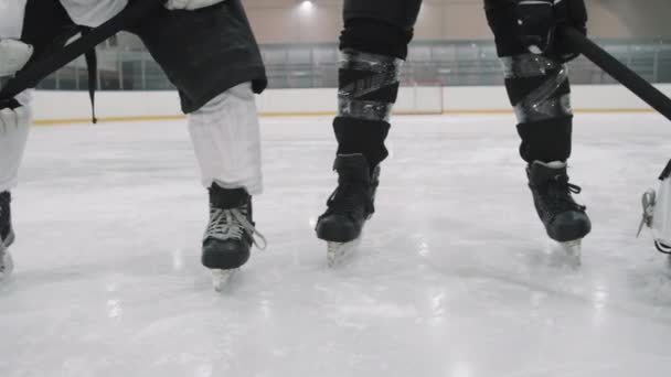 Imágenes panorámicas de baja sección de jugadores masculinos de hockey piernas en patines y equipo de protección de pie en pista de hielo en línea con portero en el medio - Metraje, vídeo
