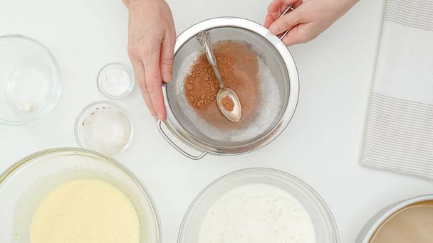 Χτυπημένα λευκά, χτυπημένοι κρόκοι και σκόνη κακάο κοντά στο τραπέζι της κουζίνας. Βήμα-βήμα συνταγή κέικ σοκολάτας, επίπεδη lay, λευκό φόντο τραπέζι κουζίνα, τα χέρια της γυναίκας - Φωτογραφία, εικόνα