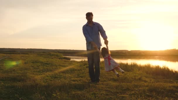 Happy family. Dad is circling a cheerful daughter, silhouette at sunset. Father and little child girl play outdoors, dad holds the babys hands and whirls in sun on beach. Family on vacation in nature - Footage, Video