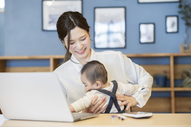 Asyalı bir kadın kucağında bebek ve içeride dizüstü bilgisayar tutuyor. - Fotoğraf, Görsel