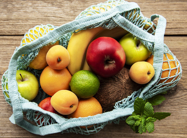 Mesh ostoskassi orgaanisia hedelmiä puinen tausta. Litteä, ylhäältä päin. Ei jätettä, muoviton konsepti. Kesähedelmät. - Valokuva, kuva