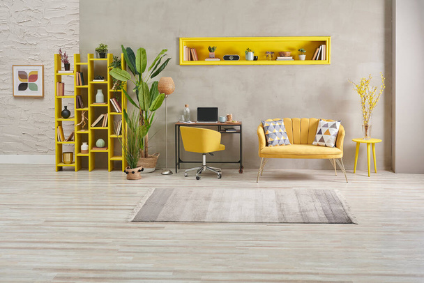 Dekorativní šedá kamenná zeď obývací pokoj, domácí interiér koncept se žlutou pohovkou a knihovnou, velká zelená váza z rostlinného koberce. - Fotografie, Obrázek