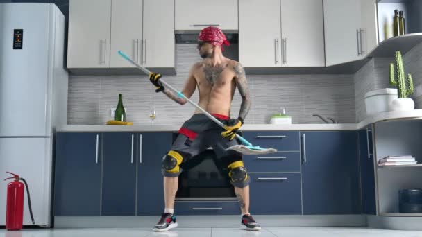 Mies, joka työskentelee siivousfirmassa, siivoaa keittiön lattian ja soittaa moppia kuin kitara. - Materiaali, video