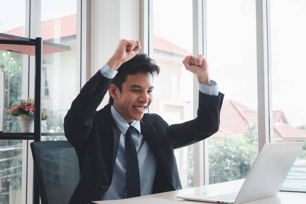 ευτυχισμένος ασιάτης επιχειρηματίας γιορτάζει την επιτυχία με τα χέρια ψηλά και ψάχνει στο laptop - Φωτογραφία, εικόνα