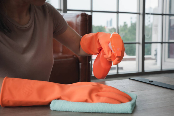 γυναίκα σε πορτοκαλί λαστιχένια γάντια με προμήθειες καθαρισμού τραπέζι - Φωτογραφία, εικόνα