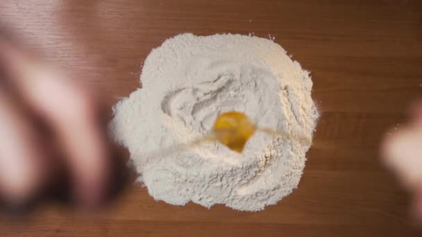 Lo chef prepara il piatto di pasta e rompe l'uovo fresco e lo getta in farina su tavolo. Le particelle di farina volano via e il tuorlo cade al centro dell'imbuto e le proteine si diffondono dal guscio ai lati. Lentamente. Vista dall'alto - Filmati, video