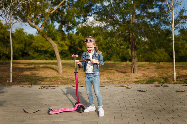 Little smiling girl with kick scooter. Happy kid playing outdoors. Carefree childhood. - Photo, Image